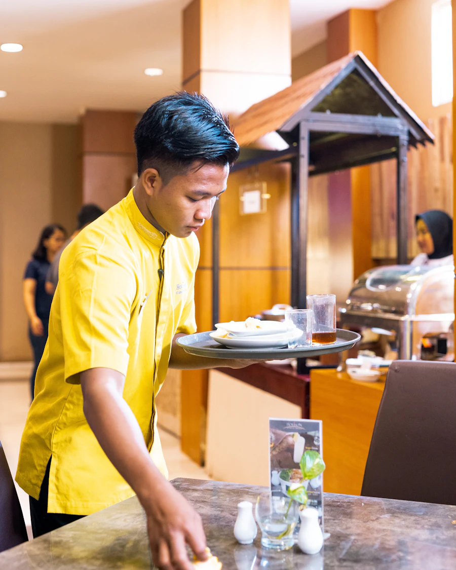 A hotel server carrying a tray across a dining room.
