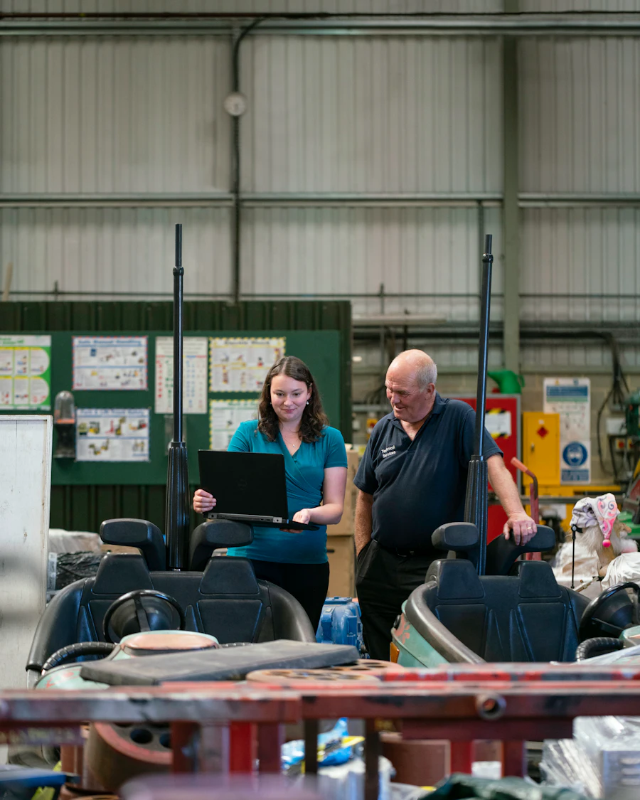 Two colleagues checking a job on a laptop on a production floor.