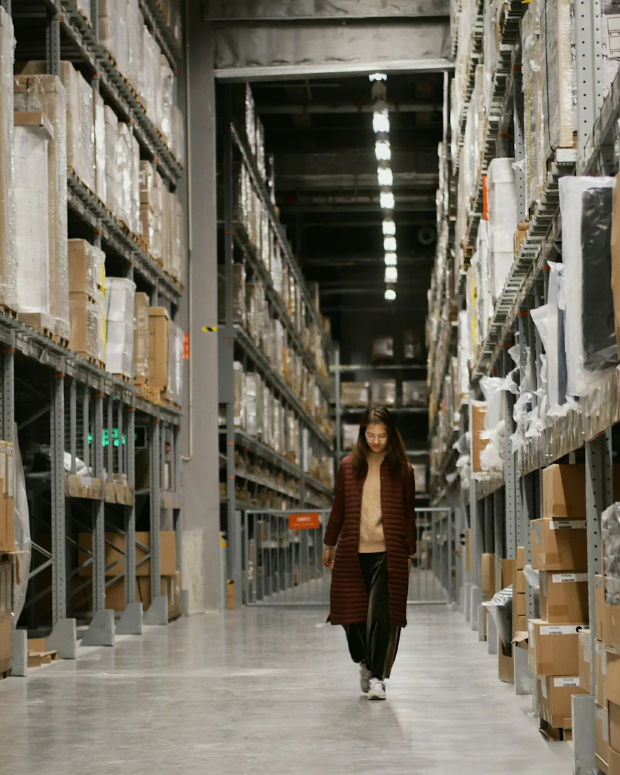A worker walking a long aisle of racked stock in a distribution center.
